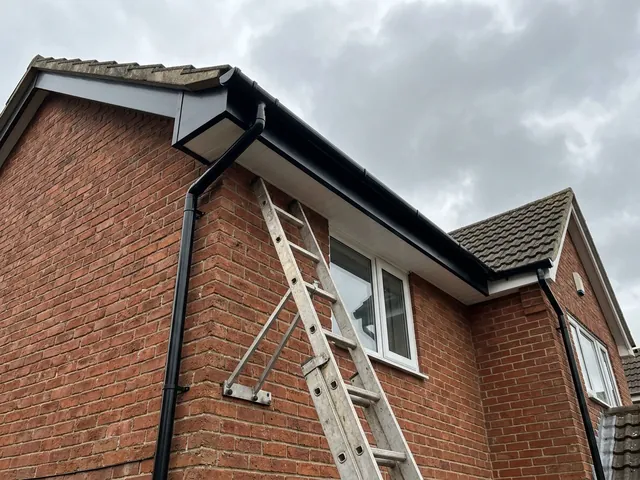 New black fascia boards, white soffits and black guttering on the corner of a brick house.